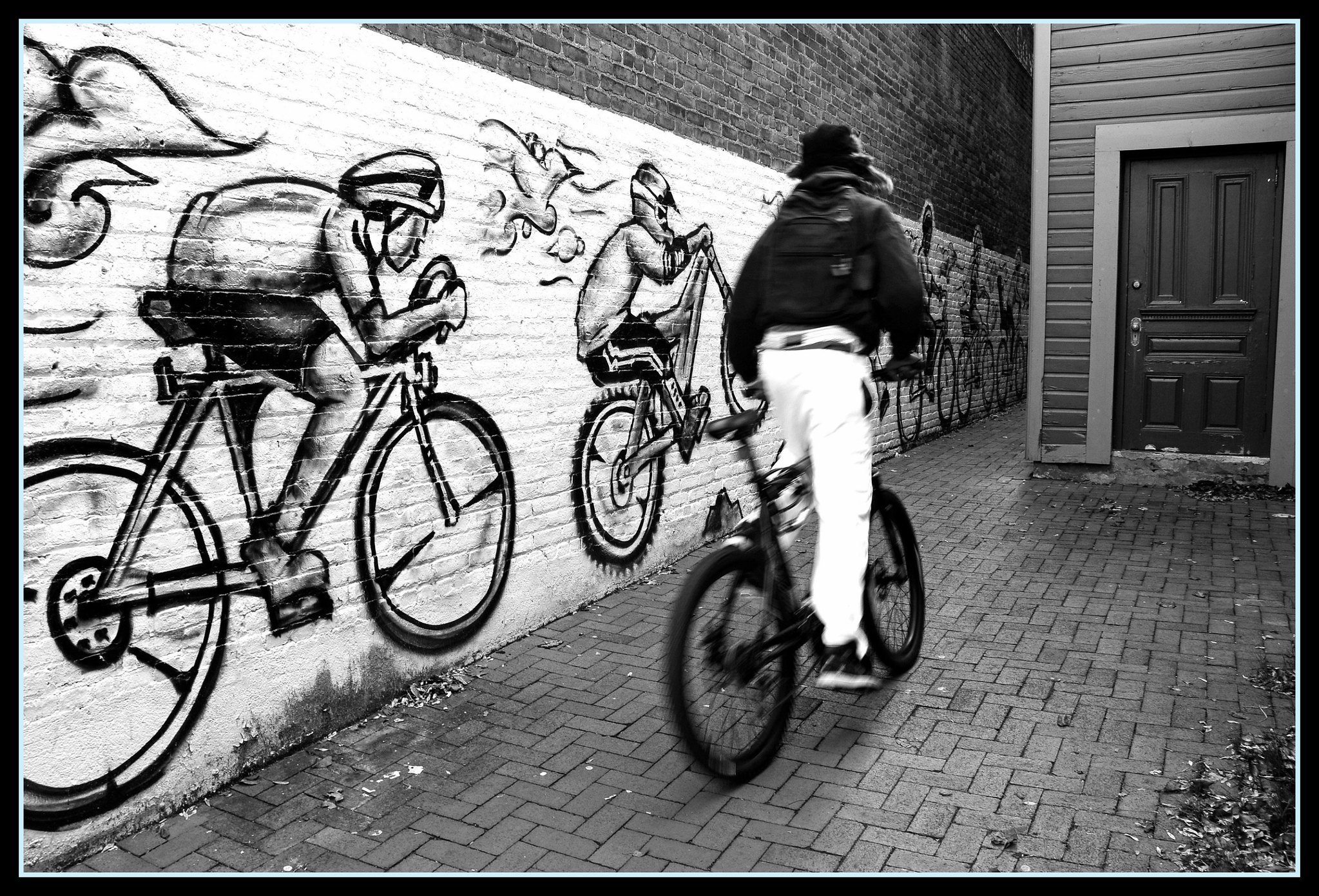 Someone biking down an alley with a mural of bikers in the background.